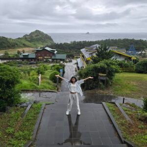 woman joyfully posing on a boardwalk overlooking lush greenry on sanbangsan and distant ocean