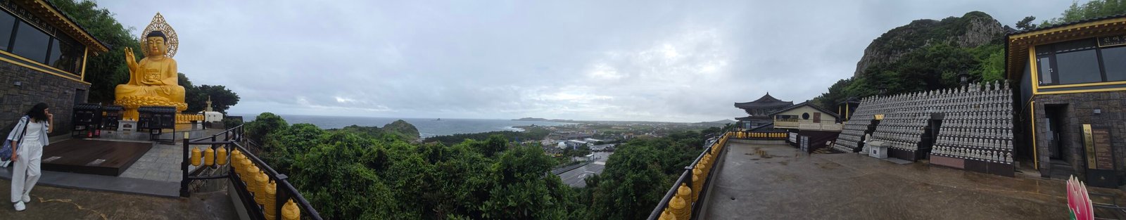 panoramic view of golden buddha statue and temple terrace overlooking sanbangsan in jeju island